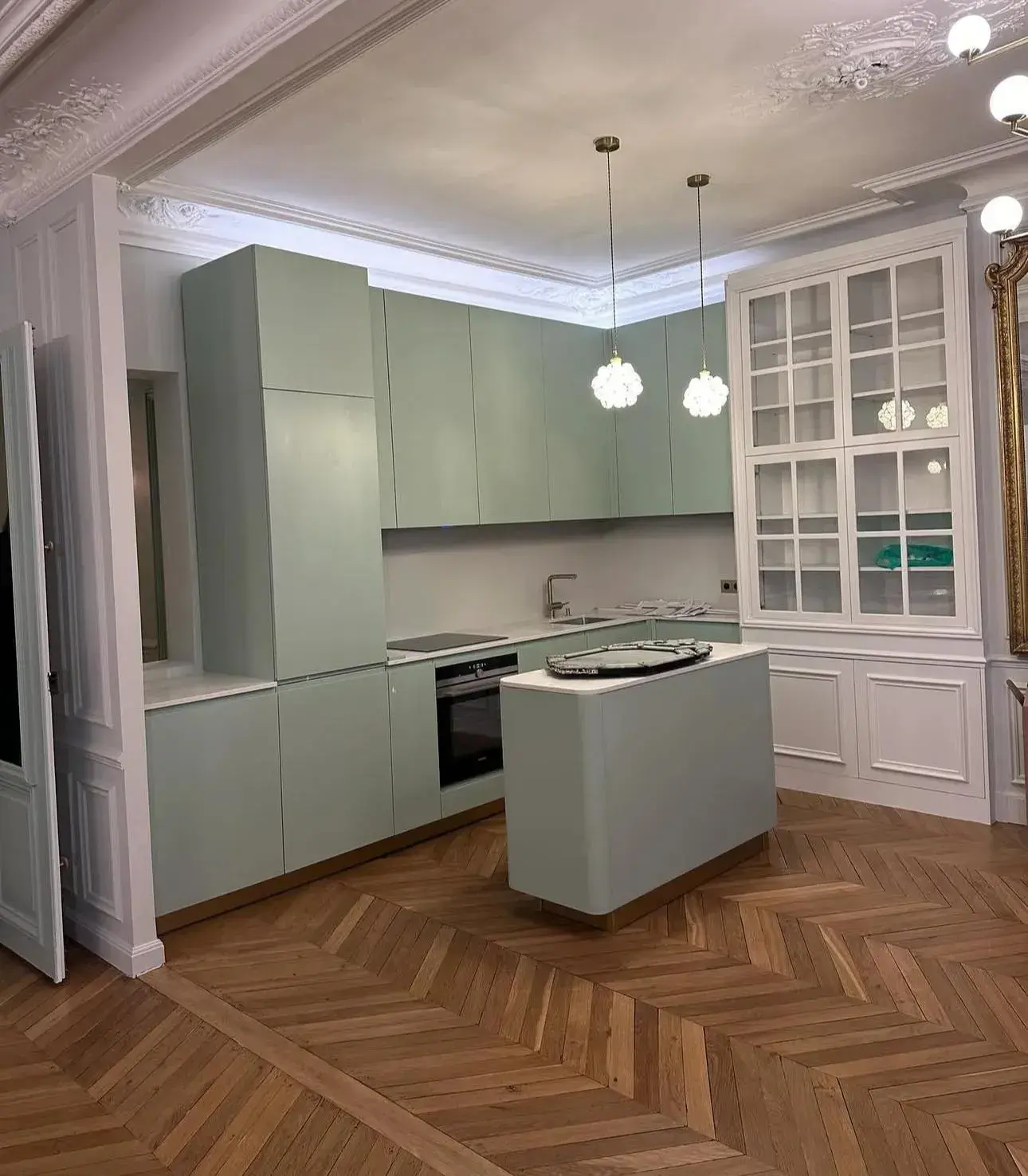 Cuisine ouverte avec îlot, façades vert clair et parquet à chevrons