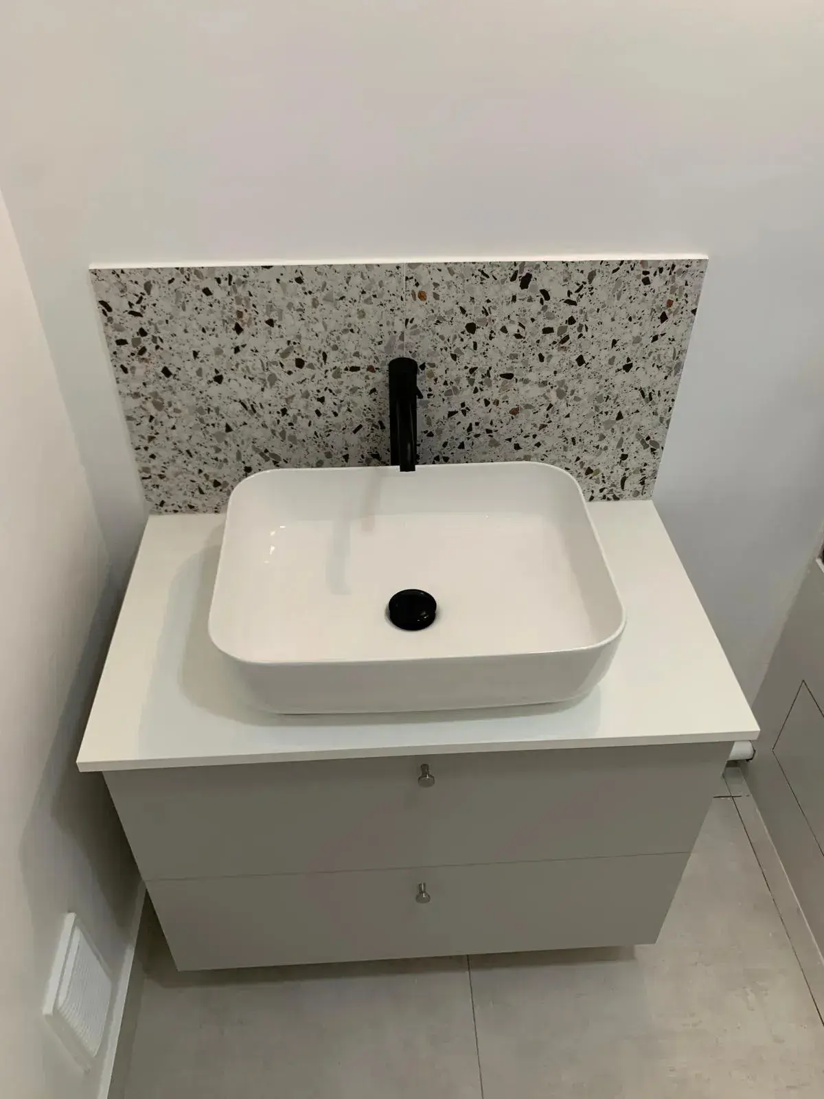 Meuble vasque suspendu gris clair avec robinet noir et crédence mouchetée