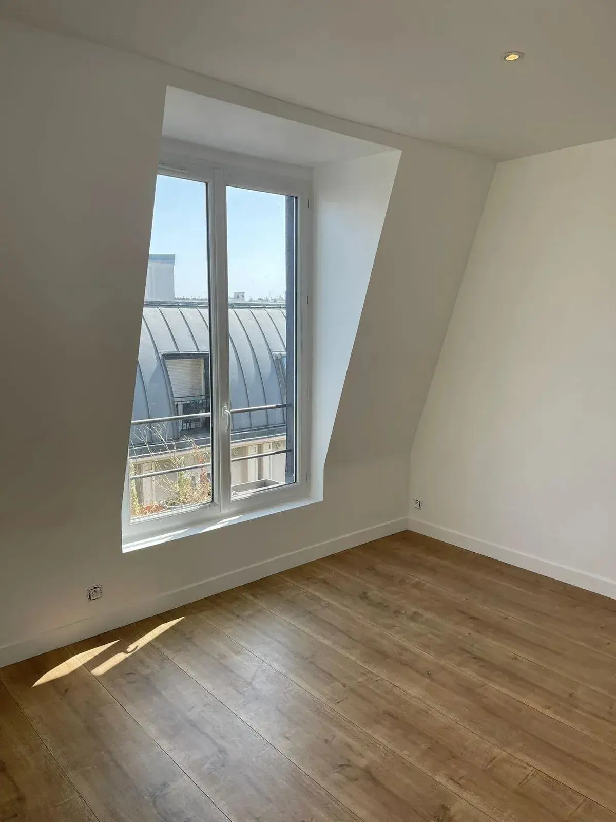 Pièce sous les toits avec murs blancs, fenêtre et lumière naturelle au sol