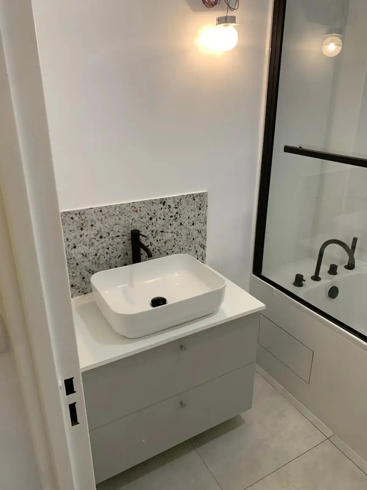 Vasque blanche, meuble gris clair et paroi de baignoire aux contours noirs