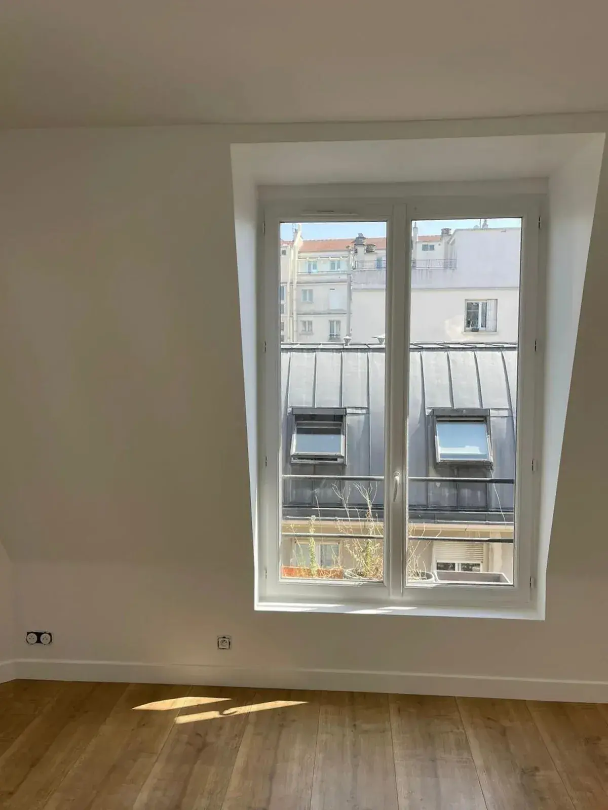Fenêtre éclairant une pièce rénovée aux murs blancs et au sol en bois